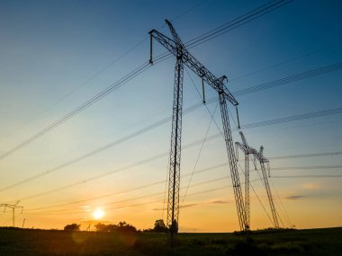 Güneş doğarken elektrik hatları olan yüksek voltajlı kulelerin koyu gölgesi.