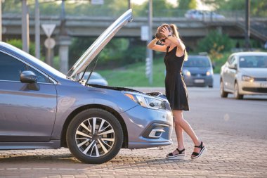 Arabasının yanında duran çaresiz kadın kaputu açık, bozuk motoru inceliyor. Genç bayan sürücünün aracıyla ilgili sorunları var