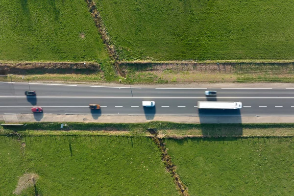 Widok z lotu ptaka na międzymiastową drogę między zielonymi polami rolniczymi z szybkimi samochodami. Widok z góry z drona ruchu drogowego — Zdjęcie stockowe