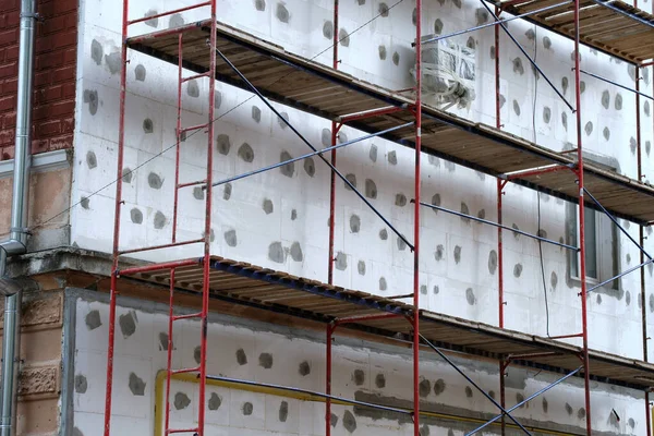 Fachada del edificio en obras de renovación con marco de andamio de construcción. Aislamiento de pared con láminas de espuma de poliestireno para un hogar eficiente —  Fotos de Stock