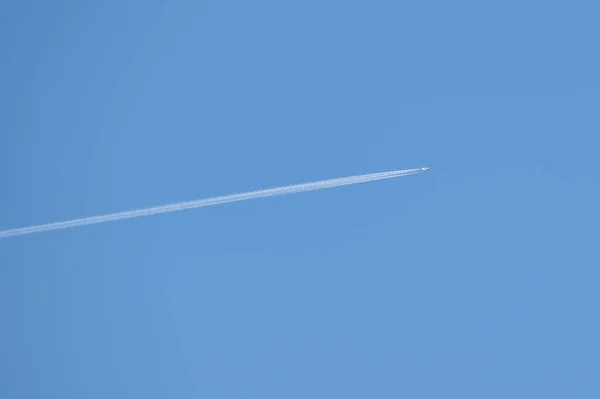 Avión a reacción de pasajeros a distancia volando a gran altitud en el cielo azul claro dejando rastro de humo blanco de la estela detrás. Concepto de transporte aéreo — Foto de Stock