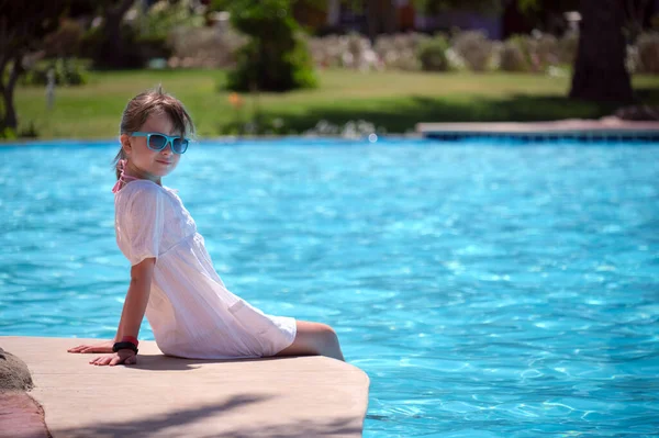 Jovem menina alegre descansando no lado da piscina com água azul clara no dia ensolarado de verão. Conceito de férias tropicais — Fotografia de Stock