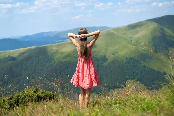 붉은 옷을 입은 젊은 여자가 더운 여름 산에서 풀 이무성 한 초원에 서서 손을 들어 자연을 보고 있다 — 스톡 사진