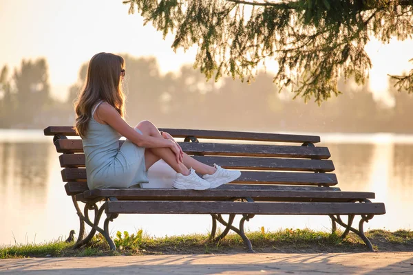 Młoda kobieta w letniej sukience siedzi zrelaksowany na ławce nad jeziorem w ciepły wieczór. Wellness odpoczynku od codziennej koncepcji szczytu — Zdjęcie stockowe