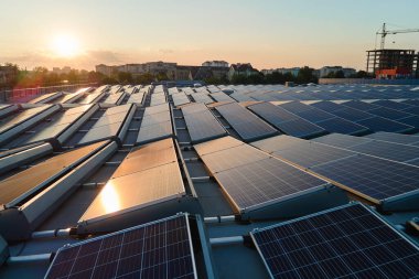 Günbatımında yeşil ekolojik elektrik üretmek için endüstriyel bina çatısına monte edilen mavi fotovoltaik güneş panellerinin hava görüntüsü. Sürdürülebilir enerji konsepti üretimi