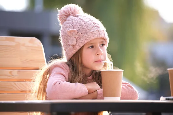 Portret van een schattig klein meisje met een roze hoed die alleen op straat thee drinkt uit een bekertje. — Stockfoto