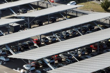 Güneş panellerinin hava görüntüsü park yerinin üzerine gölge çatısı olarak yerleştirilmiş ve temiz elektriğin etkin üretimi için park edilmiş arabalar var. Fotovoltaik teknoloji şehir altyapısına entegre edildi
