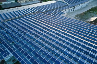 Sanayi binasının çatısına yeşil ekolojik elektrik üretmek için monte edilmiş mavi fotovoltaik panelli güneş enerjisi santralinin hava görüntüsü. Sürdürülebilir enerji konsepti üretimi