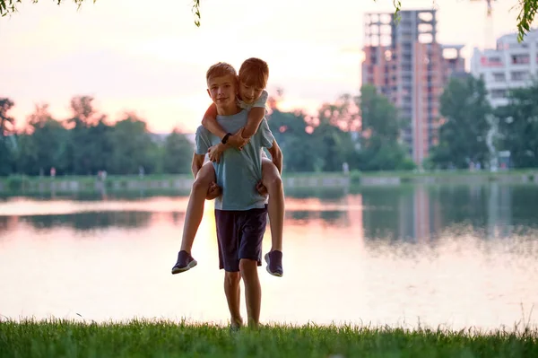 Счастливые братья и сёстры обнимаются в летнем парке. Маленькие дети брат и сестра обнимают друг друга на открытом воздухе. Концепция семейной любви и отношений — стоковое фото