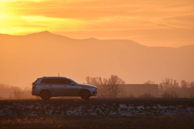 Gün batımında şehirlerarası yolda hızla giden bir SUV arabası. Akşamları otoyol trafiği