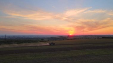 Gün batımında tarım sahasında böcek öldürücü kimyasallar püskürten traktör..