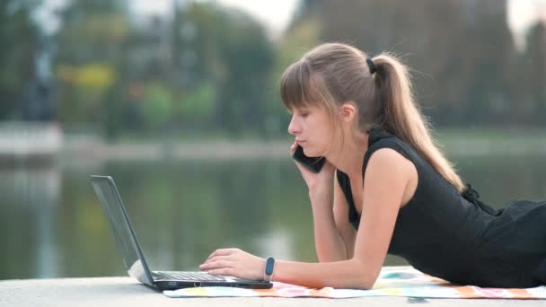 在室外的夏季公园里 一个愤怒的女人一边在手提电脑后面工作 一边生气地一边用手机说话 远程工作概念 — 图库视频影像