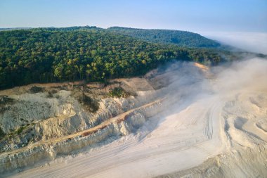Kazı araçları ve çöp kamyonları ile inşaat endüstrisi için kireçtaşı malzemelerinin açık çukur madenciliğinin hava görüntüsü.