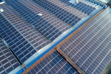 Sanayi binasının çatısına yeşil ekolojik elektrik üretmek için monte edilmiş mavi fotovoltaik panelli güneş enerjisi santralinin hava görüntüsü. Sürdürülebilir enerji konsepti üretimi.