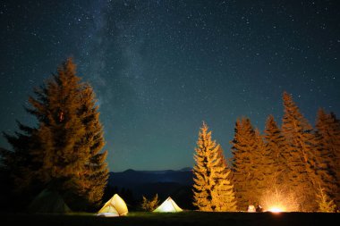 Parlak turist çadırları, gece gökyüzünün altındaki karanlık dağlarda, parlayan yıldızlarla parlayan kamp alanlarında. Etkin yaşam tarzı kavramı.