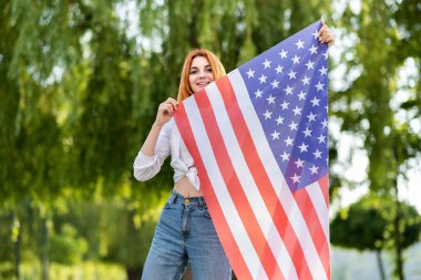 Yaz parkında Amerikan bayrağıyla poz veren mutlu genç kız. Açık havada afişi olan pozitif genç bir kadın..