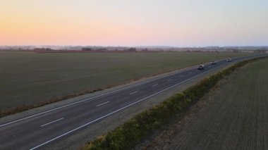 Gün batımında hızlı giden arabalarla şehirlerarası yol manzarası. Akşamları otoban trafiğinin insansız hava aracı görüntüsü.