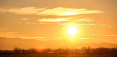 Güzel bir akşam panoramik manzarası. Gün batımında uzak dağ tepeleri üzerinde parlak batan güneş..