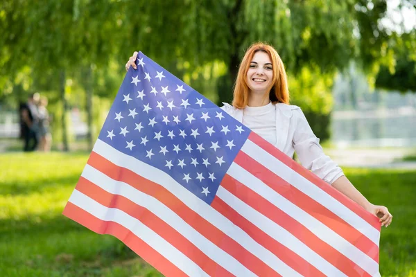 Szczęśliwa Młoda Rudowłosa Kobieta Pozująca Flagą Usa Stojącą Świeżym Powietrzu — Zdjęcie stockowe