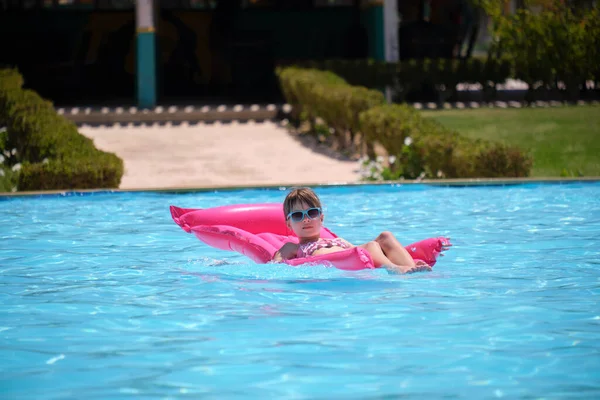 Genç kız tropik tatiller sırasında yüzme havuzunda şişme şişme yatakta yüzerek yaz güneşinde dinleniyor. Yaz etkinlikleri konsepti.