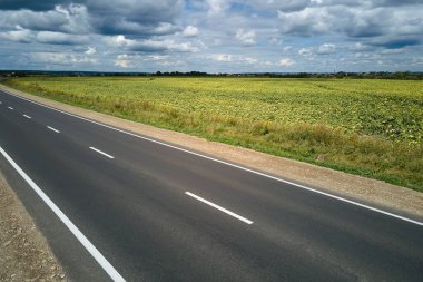 Yeşil tarım alanları arasındaki boş şehirlerarası yolun havadan görünüşü. Karayolu insansız hava aracının üst görüntüsü.