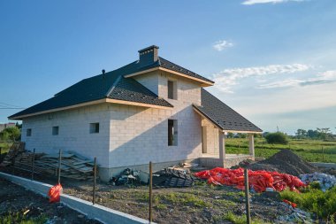 Havalandırılmış hafif beton duvarları ve inşaat halindeki metalik fayanslarla kaplı ahşap çatı iskeleti olan bitmemiş evin havadan görüntüsü..