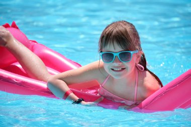 Genç neşeli kız tropikal tatillerde sıcak yaz gününde mavi suyla yüzme havuzunda şişme şişme yatakta yüzerken eğleniyor. Yaz etkinlikleri konsepti.