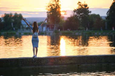 Yalnız genç bir kadının gölde tek başına dikilip sıcak bir akşamın tadını çıkarırken ellerini kaldırışının arkası. Başarı ve meditasyon kavramı.
