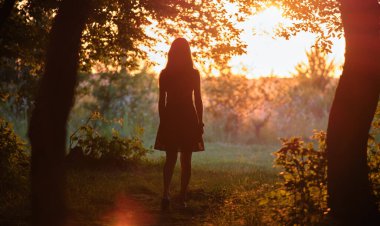 Gün batımında karanlık ormanda tek başına yürüyen genç bir kadın. Doğa keşfi kavramı.