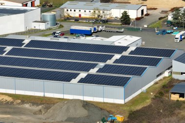 Sanayi binasının çatısına yeşil ekolojik elektrik üretmek için monte edilen mavi fotovoltaik güneş panellerinin hava görüntüsü. Sürdürülebilir enerji konsepti üretimi.