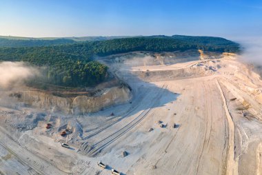 Kazı araçları ve çöp kamyonları ile inşaat endüstrisi için kireçtaşı malzemelerinin açık çukur madenciliğinin hava görüntüsü.