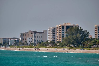 Beyaz kumları, mavi suları, yüksek otel binaları olan bir tatil köyü. Mutlu insanlar güneşleniyor ve okyanusta yüzüyor..