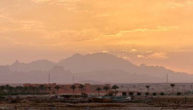 Uzak otel kompleksiyle gün batımı manzarası Mısır çölündeki karanlık dağ zirvelerine karşı.