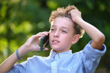 Yazlık parkta cep telefonuyla konuşan kafası karışmış bir çocuk..