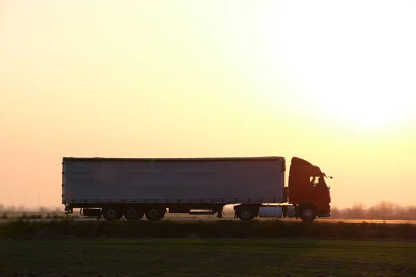 Semi-truck with cargo trailer driving on highway hauling goods in evening. Delivery transportation and logistics concept.