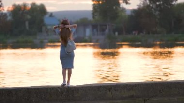 Sıcak bir akşamda göl kenarında rahatlayan günlük kıyafetli genç bir kadın. Yaz tatilleri ve seyahat konsepti.