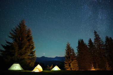 Parlak turist çadırları gece gökyüzünün altındaki karanlık dağlarda parlayan parlayan yıldızlarla. Etkin yaşam tarzı kavramı.