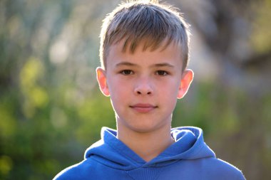 Yeşil, güneşli arka planda kameraya gülümseyen sıradan giyinmiş yakışıklı bir gencin portresi..