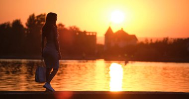 Sıcak bir akşamda göl kıyısında tek başına duran yalnız bir kadın. Yalnızlık ve doğa konseptinde rahatlama..