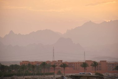 Uzak otel kompleksiyle gün batımı manzarası Mısır çölündeki karanlık dağ zirvelerine karşı.