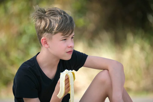 年轻英俊的男孩在户外吃着美味的成熟香蕉 — 图库照片