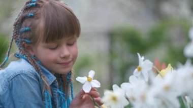 Mutlu kız çocuğu yaz bahçesinde oynuyor güneşli bir günde beyaz narsislerin tatlı kokusunun tadını çıkarıyor..