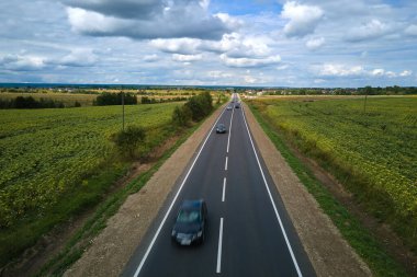 Hızlı giden arabalarla yeşil tarımsal alanlar arasındaki şehirlerarası yolun havadan görünüşü. Karayolu trafiğinin insansız hava aracı görüntüsü.