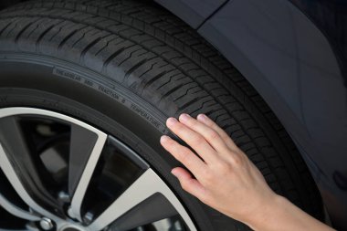 Kadın sürücü elleri yeni arabasının tekerlek lastiklerini inceliyor. Araç güvenliği kavramı.