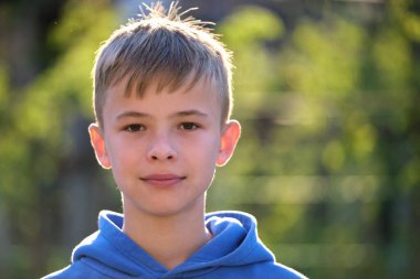 Yeşil, güneşli arka planda kameraya gülümseyen sıradan giyinmiş yakışıklı bir gencin portresi..