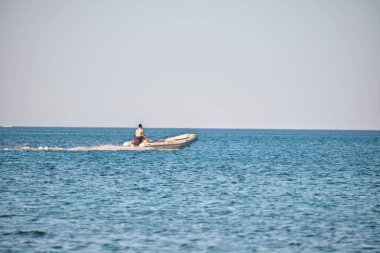 Mavi deniz suyunun dalgalı yüzeyi ve durgun dalgalarda hızlı yüzen beyaz sürat teknesiyle deniz manzarası..