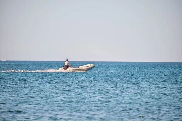Mavi deniz suyunun dalgalı yüzeyi ve durgun dalgalarda hızlı yüzen beyaz sürat teknesiyle deniz manzarası..