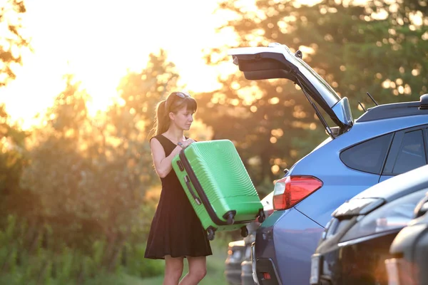 Young woman driver taking out suitcase bag out of her car. Travelling and vacations concept.