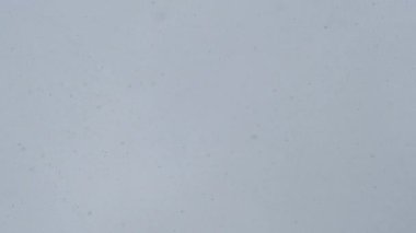 Kış günü düşen kar tanelerinin gri bulutlu gökyüzüne karşı soyut görünümü.
