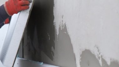 İnşaat işçisi termal koruma için evin ön cephesine köpük yalıtım çarşafları yerleştiriyor..